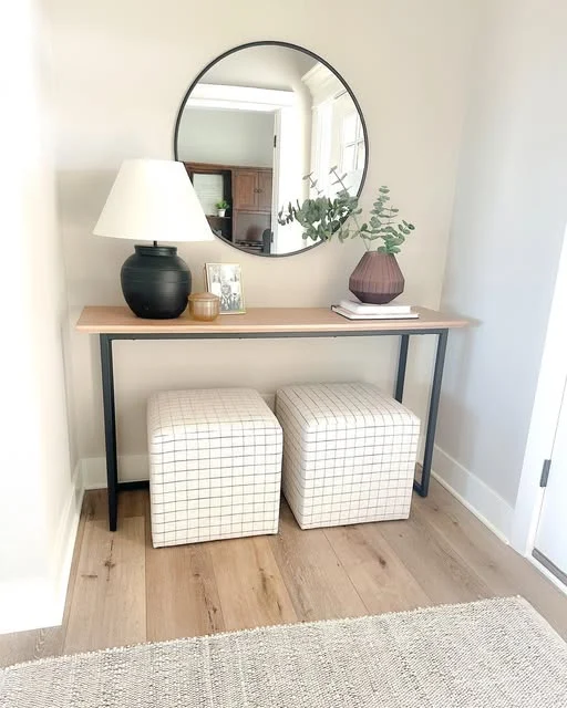 Entry console with a round mirror, greenery, lamp, and two upholstered stools