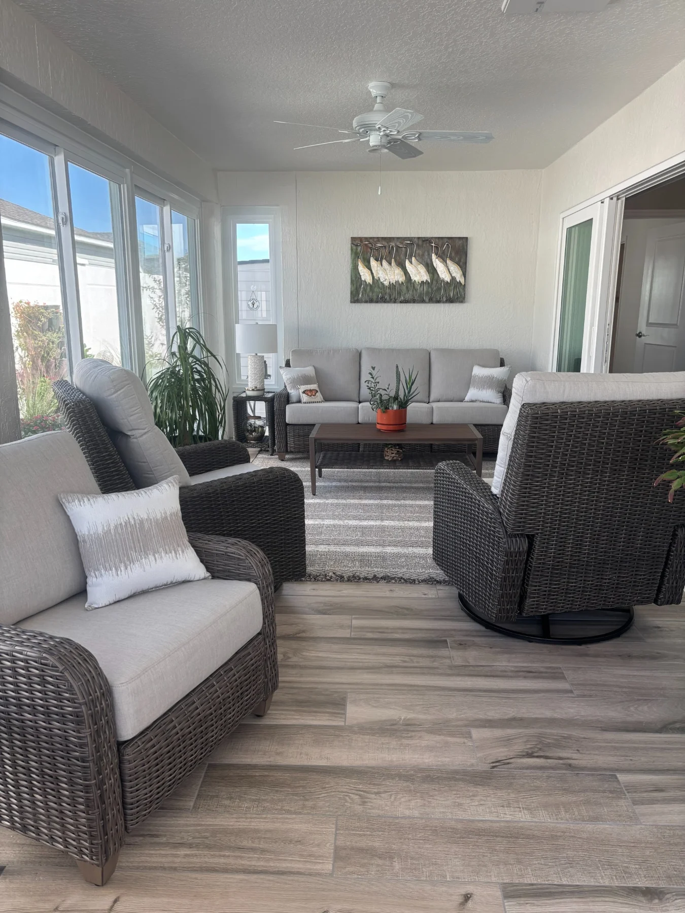 Enclosed lanai with woven lounge chairs, soft neutral cushions, and a seating area beside tall windows