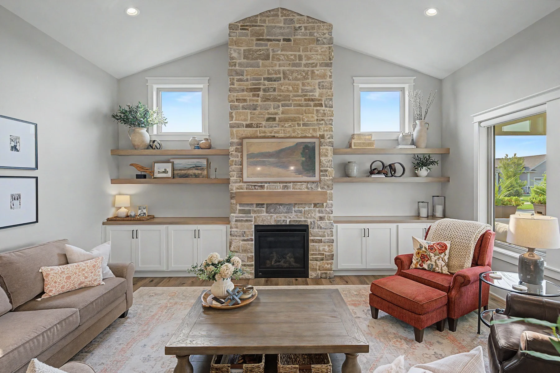 Light-filled living room with a stone fireplace, layered neutral furnishings, and a rust accent chair